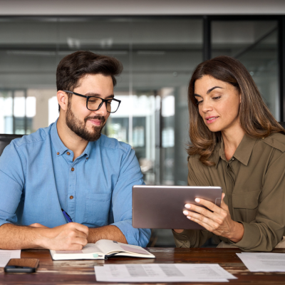 Man and woman sat at a desk looking at an ipad